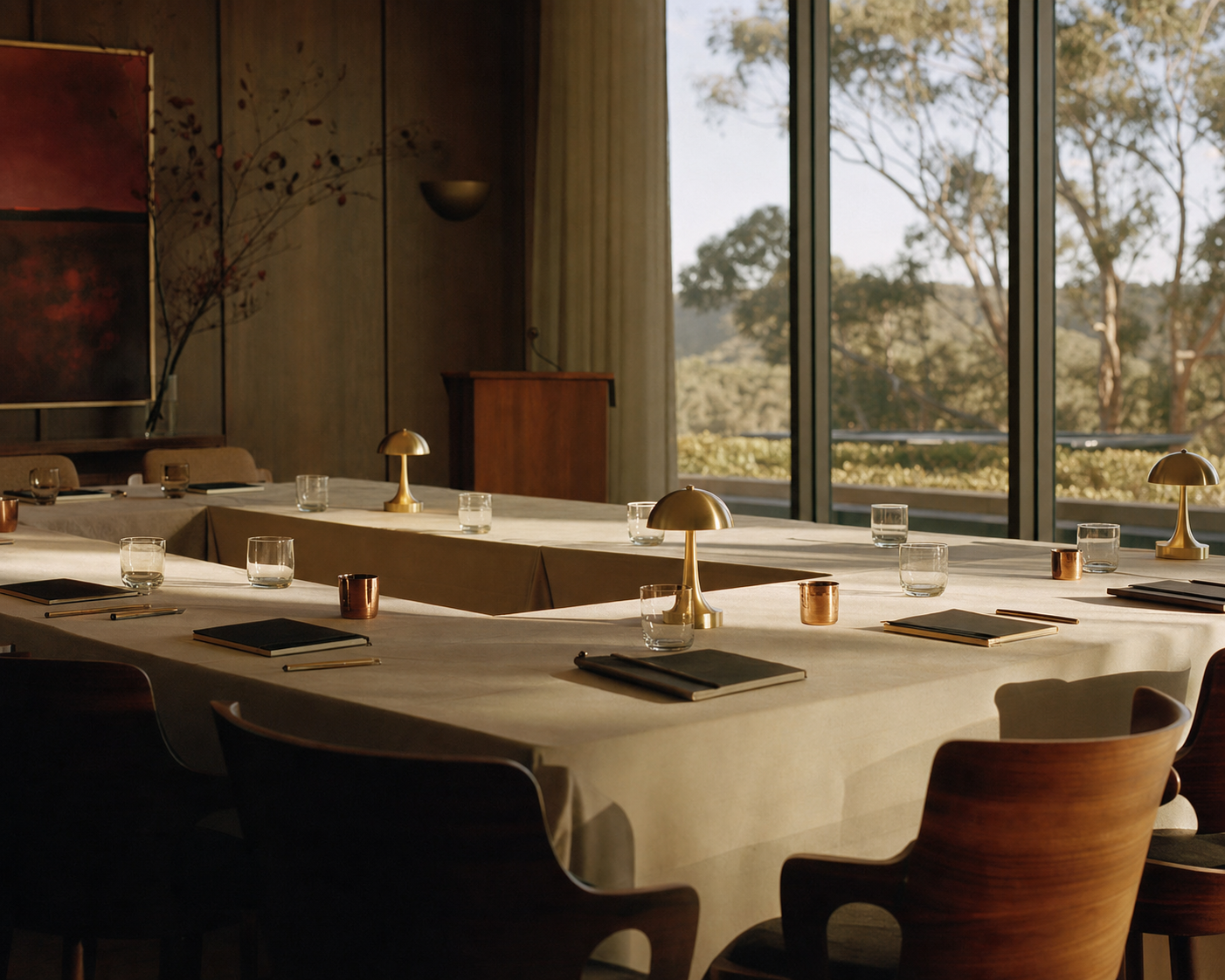 An intimate professional gathering room at golden hour, set with walnut tables, brass lamps, and cream linens